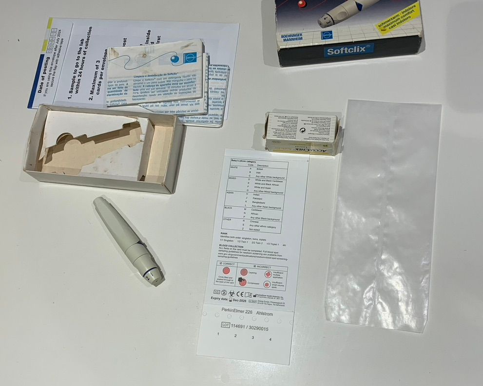 A set up for taking PKU blood spots including absorbent testing card, wax and posting envelopes, and a lancet Softclix device.