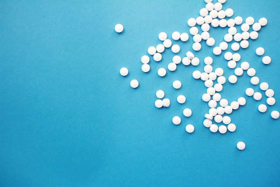 Small white pills strewn across a blank teal background.