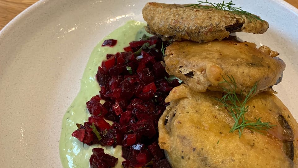 3 individual mushroom & jackfruit wellingtons grilled to a bright yellow stacked on a plate with beetroot salad on the side