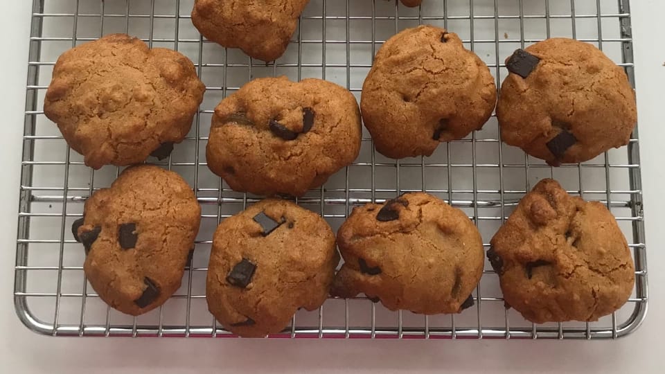 A wire baking rack holding eight cookies baked to a bright orange with dark chocolate chunks melted throughout