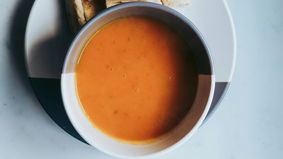 Photo by Sandie Clarke / Unsplash. Close up of an orange coloured, blended carrot soup in a two tone bowl.